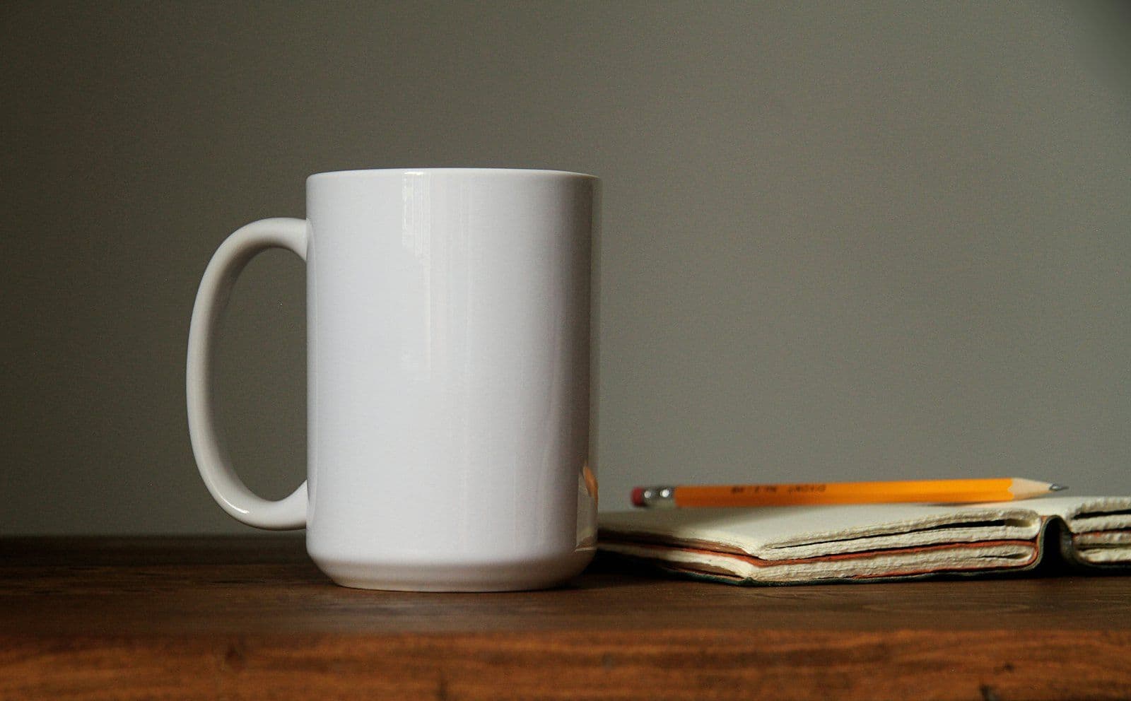 A white mug beside an orange pencil on an open notebook