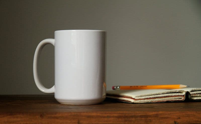 A white mug beside an orange pencil on an open notebook